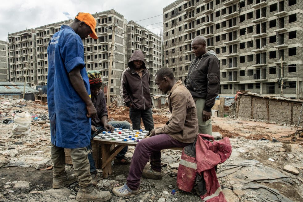 Des habitants de Soweto Zone D jouent aux dames au milieu des vestiges de maisons démolies, devant des bâtiments en construction dans le cadre d’un programme public de logements abordables, à la suite de démolitions planifiées par le gouvernement pour faire place au projet dans le bidonville de Kibera, à Nairobi, au Kenya, le 23 avril 2026.